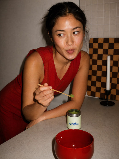 Woman with a matcha spoon and a tin of Jondal matcha in the kitchen