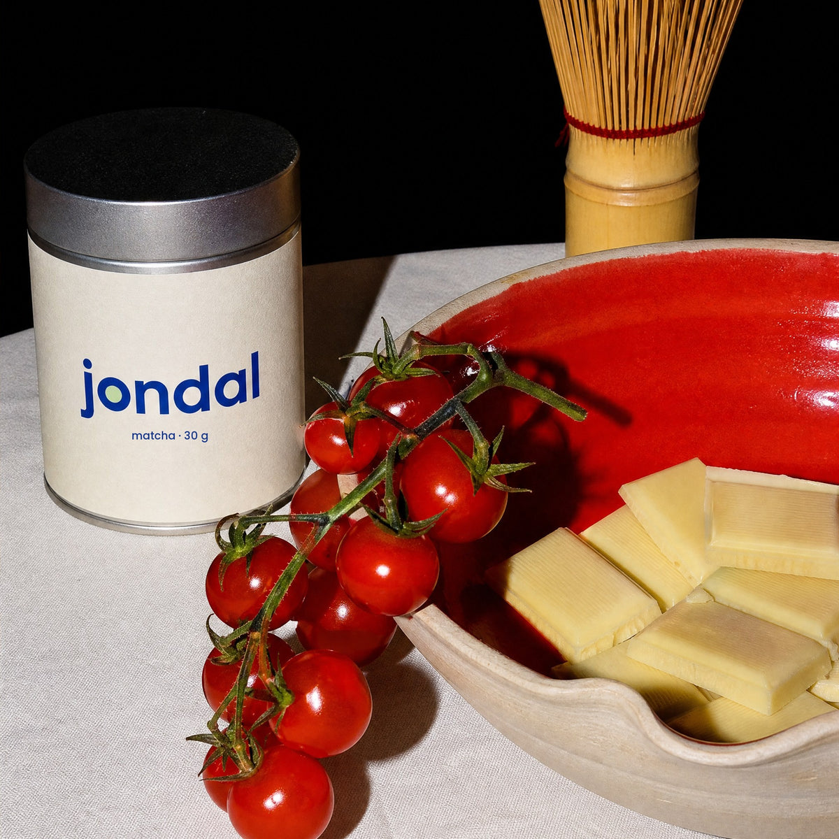 Tin of Jondal matcha 30 g on a linen table with cherry tomatoes and a red bowl