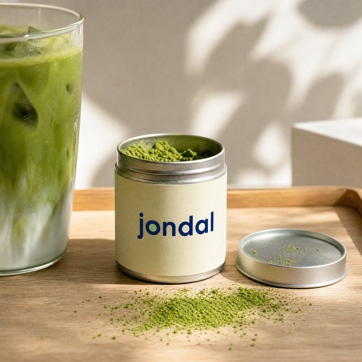 Open tin of Jondal matcha next to an iced matcha latte